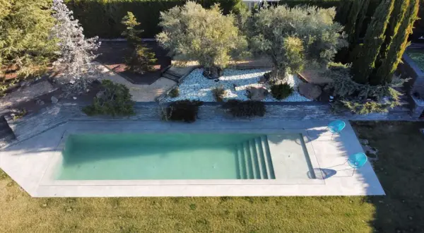 Piscina moderna de obra con escaleras integradas, rodeada de jardín con olivos y cipreses. Un ejemplo de los diversos tipos de piscinas de obra.