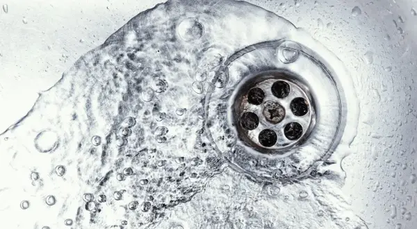 Wasser fließt in einen verstopften Abfluss. Vielleicht hilft ein Gebissreiniger, die Ablagerungen zu lösen.