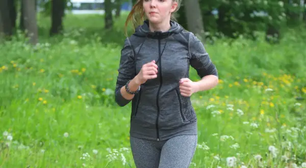 Twarz biegaczki skupiona na celu, w tle zielony park z żółtymi kwiatami.