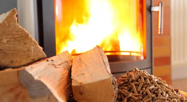 Cheminée avec un feu vif. À gauche, des bûches de bois. À droite, un tas de granulés. Un insert mixte bois et granulés, avis sur le rendement.