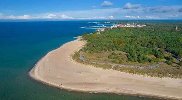 Półwysep Helski: piaszczysta plaża, turkusowe morze i las. W oddali widać miasteczko i port. Atrakcje tego miejsca zachwycają.