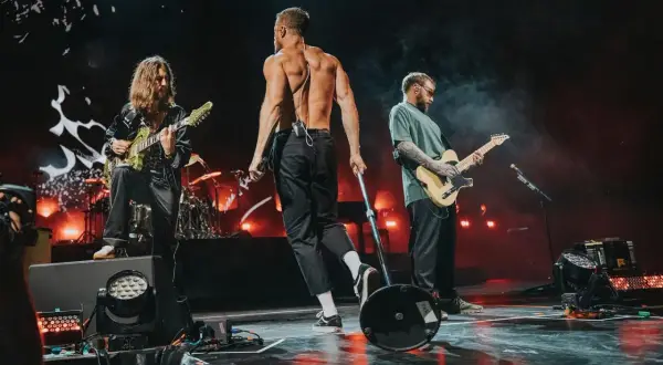 Imagine Dragons na koncercie w Polsce: wokalista bez koszulki, gitarzyści grający na scenie.
