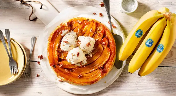 Eine köstliche gebackene Banane Tarte mit Vanilleeis und Pekannüssen, daneben frische Chiquita Bananen.