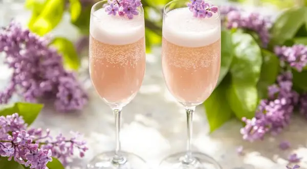 Två glas med rosa bubbel, dekorerade med syrenblommor. Perfekt för ett syrensirap recept.