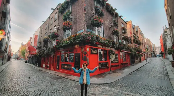 Kobieta pozuje przed słynnym pubem The Temple Bar w Dublinie, stolicy Irlandii. Uliczka wybrukowana kocimi łbami.