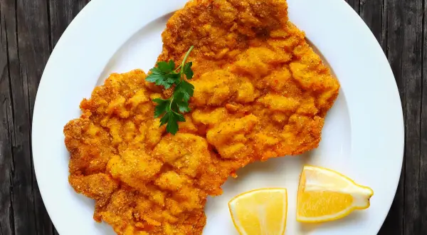 Ein knuspriges Wiener Schnitzel auf weißem Teller, garniert mit Petersilie und Zitronenspalten. Perfekt für einen herzhaften Genuss.