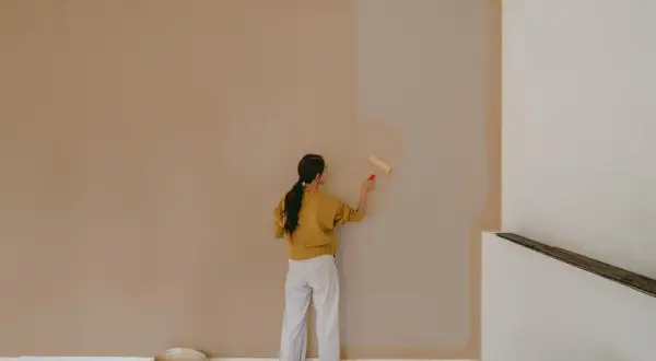 Frau streicht Wand mit neuer Farbe. Die Frage, wie lange braucht Wandfarbe zum trocknen, beschäftigt sie.