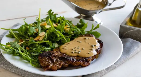 Un succulento filetto al pepe verde, nappato con salsa cremosa, servito con un'insalata fresca di rucola e mandorle.
