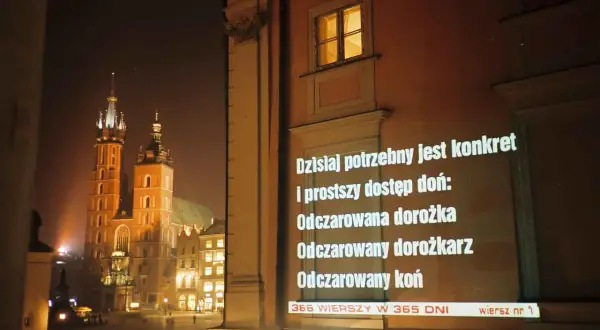 Nocny Kraków. Na ścianie budynku wyświetlane są wiersze o krakowie, m.in. o odczarowanej dorożce.
