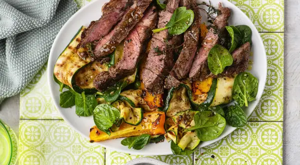 Pokrojony, soczysty sirloin steak z grillowanymi warzywami: cukinią, papryką i szpinakiem, udekorowany świeżym tymiankiem.