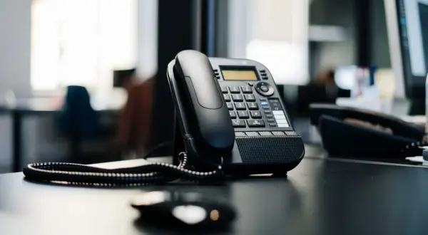 Czarny telefon biurowy na biurku. Słychać dzwonek, jakby numer zablokowany dzwonił, ale nikt nie odbiera.