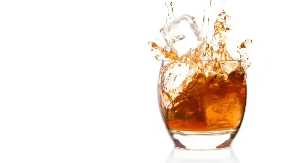 Bursztynowa whisky z lodem rozpryskuje się w szkle. Czy whisky podnosi ciśnienie? To pytanie pozostaje otwarte, gdy patrzymy na ten dynamiczny obraz.