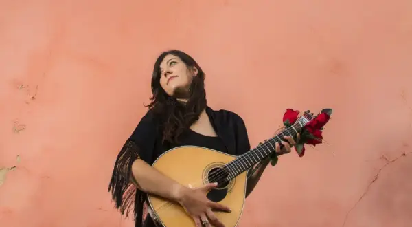 Młoda kobieta z gitarą, ozdobioną czerwonymi różami, przypomina duchem Amalię Rodrigues, legendę fado.