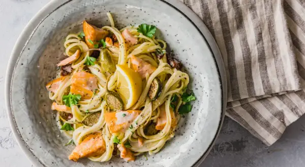 Ein Teller mit cremigen Nudeln mit Lachs, garniert mit Zitrone und Petersilie.
