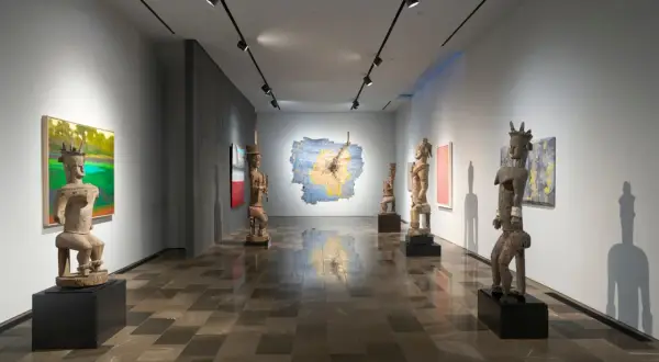 Osman Can Yerebakan's exhibition features striking wooden sculptures and vibrant paintings in a modern gallery space.