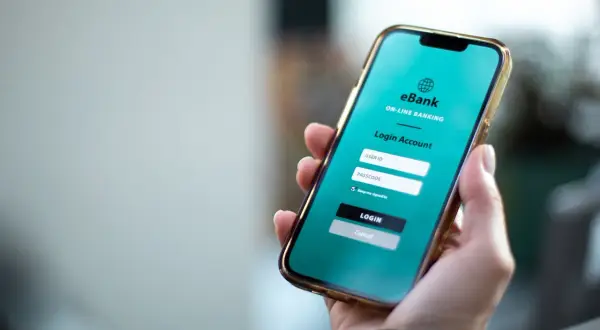 Dłoń trzyma smartfon z aplikacją bankową. Widoczny ekran logowania, gdzie można wpisać dane do konta. Gdy karta czasowo zablokowana PKO, jak odblokować? Sprawdź w aplikacji.