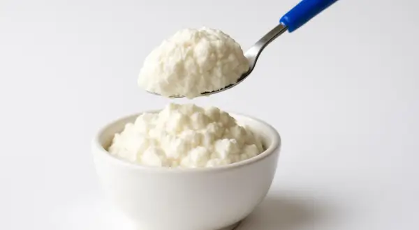 Ricotta fresca in una ciotola, con un cucchiaio che ne preleva una porzione. Un alimento leggero, ideale per chi controlla il colesterolo.