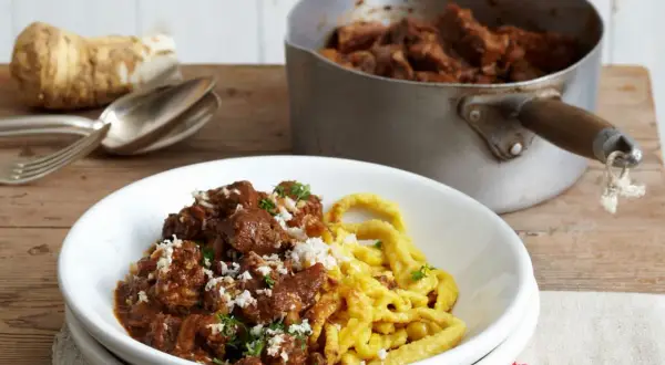 Zartes Gulasch mit Spätzle, garniert mit frischer Petersilie und geriebenem Meerrettich. So wird Gulasch zart!