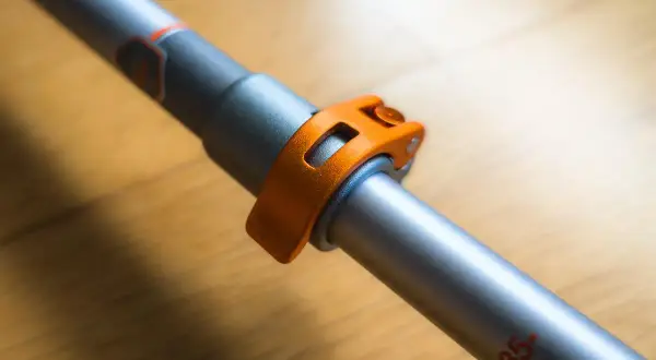 Gros plan sur le mécanisme de serrage orange d'un bâton de marche pliable ou télescopique, prêt pour l'aventure.