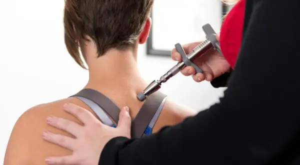 Thérapeute utilisant un appareil pour soulager la douleur haut du dos gauche d'une patiente.