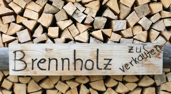 Holzstapel mit einem Schild "Brennholz zu verkaufen". Das Holz ist gespalten und bereit für den Winter, ob esche oder buche.
