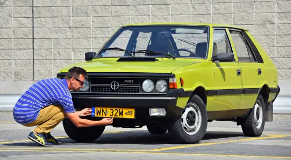 Mężczyzna przykręca żółtą tablicę rejestracyjną do zielonego Poloneza. Czy to auto ma już ile lat musi mieć auto na zabytek?