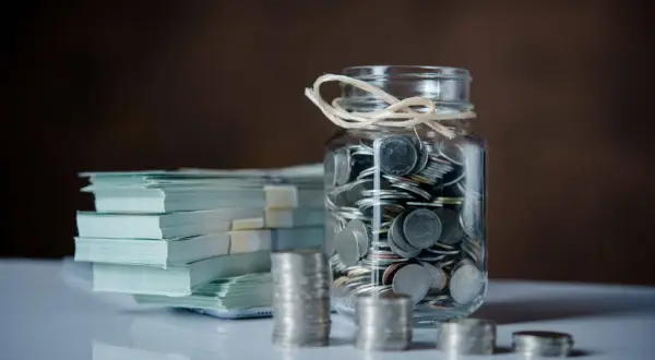 Stos banknotów i słoik pełen monet. Zastanawiasz się, jak zapłacić podatek od darowizny od obcej osoby?