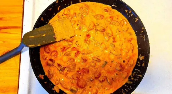 En stekpanna med krämig korv stroganoff bubblar. En spatel lyfter upp en bit av den läckra grytan.