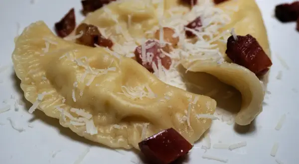 Pierogi, en klassisk polsk mat, serveras med riven ost och tärnat fläsk.
