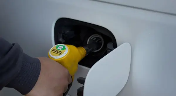 Ręka trzymająca żółtą dyszę dystrybutora z napisem DIESEL B10, tankująca samochód.