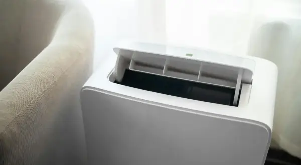 Nowoczesny klimatyzator bez jednostki zewnętrznej, z otwartą klapą wentylacyjną, obok jasnej kanapy.
