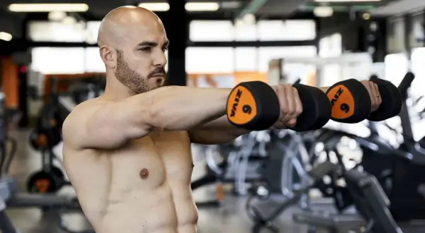 Uomo con manubri in palestra, parte di una scheda multifrequenza 4 giorni.
