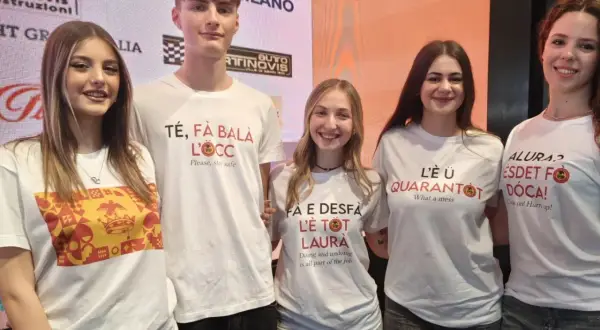 Cinque giovani sorridono, indossando magliette con scritte in dialetto. Una dice "Té, fà balà l'oeucc", che significa "Ti faccio l'occhiolino", un invito a prendersi cura di sé.