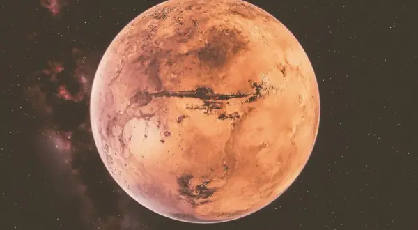 Czerwona planeta Mars, z widocznymi kraterami i kanionami, na tle gwiezdnego nieba. W tle widać mgławice, które mogą sugerować retrogradację Marsa.