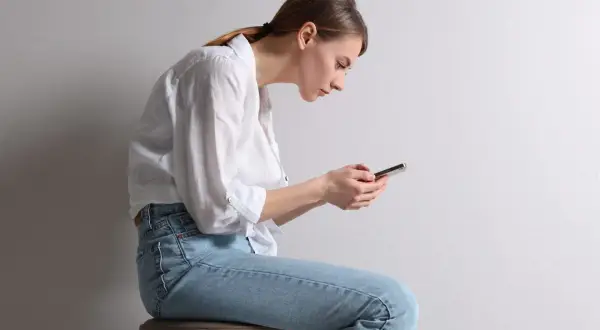 Frau mit schlechter Haltung, die auf ihr Handy schaut. Ihr Rücken ist gekrümmt, was zu einem Buckel am Nacken führt.