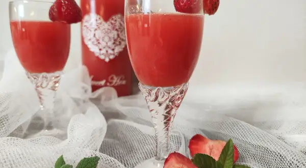 Dwa kieliszki z orzeźwiającym, czerwonym drinkiem, ozdobione truskawkami. Obok butelka z napisem "Sweet Heart", sugerująca pyszny alkohol truskawkowy.