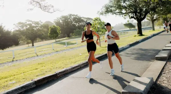 Deux femmes profitent d'un entraînement de course à pied matinal dans un parc verdoyant, leurs sourires reflétant leur plaisir.