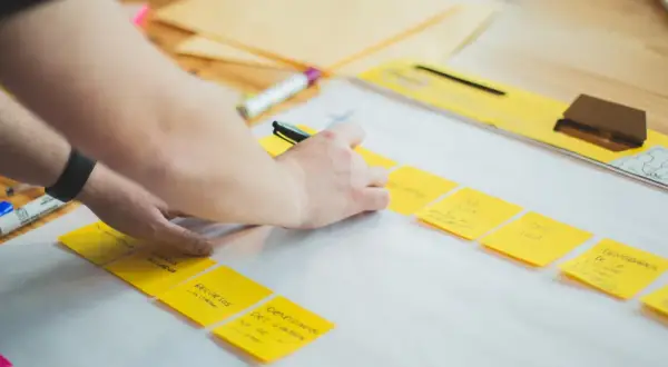 Ręce układają żółte karteczki z notatkami, tworząc mapę myśli. To kluczowy etap planowania strategii firmy.