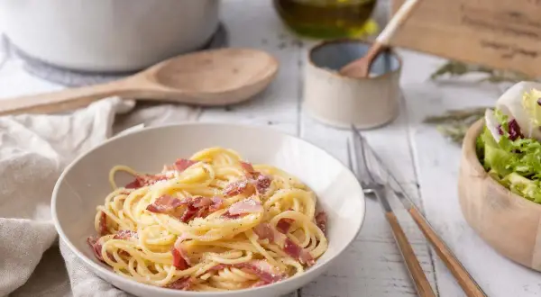 Un plat de spaghetti crémeux, garni de lardons croustillants, évoque la vraie recette carbonara italienne. Une salade fraîche accompagne ce délice.