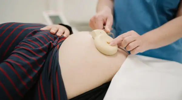 Une main ajuste un moniteur sur le ventre d'une femme enceinte. Apprendre à comment lire un monitoring est essentiel pour le suivi de grossesse.