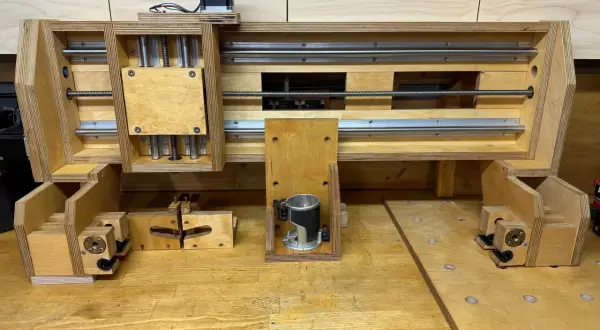 Domowa frezarka CNC DIY z drewna i metalowych prowadnic. Widać silnik krokowy, wrzeciono z frezarką ręczną i mechanizm śrubowy.