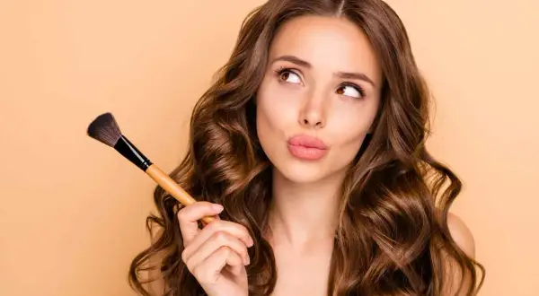 Ragazza con pennello da trucco, pensierosa, mentre impara a truccarsi.