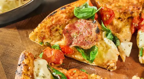 En härlig pizza Parma med salami, tomater och färsk basilika på en träskärbräda.