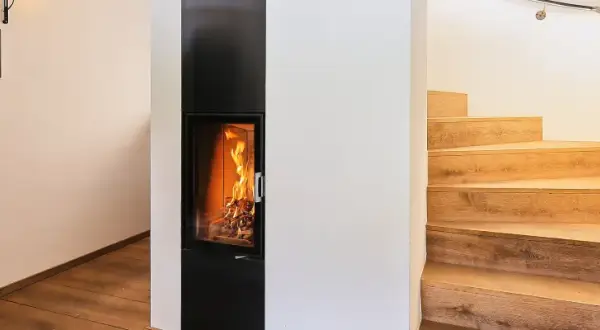 Ein moderner Kamin mit brennendem Feuer, daneben eine Holztreppe. Hier sieht man, was ein Grundofen leisten kann: Wärme und Gemütlichkeit.