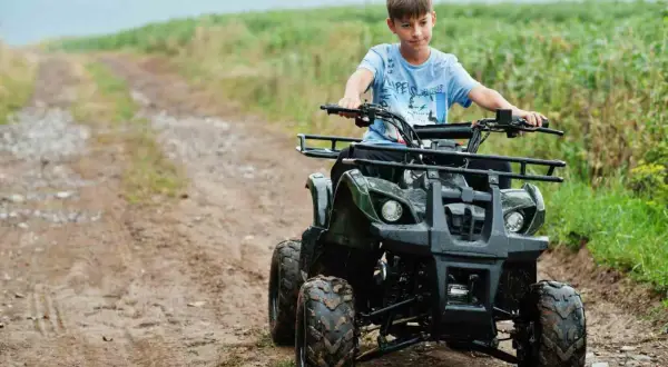 Chłopiec na quadzie, kategoria B1, jedzie po błotnistej drodze wśród zielonych pól.