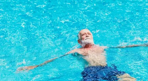 Ein älterer Mann mit Bart entspannt sich im Wasser. Schwimmen bei Arthrose kann Linderung verschaffen.