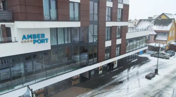 Nowoczesny hotel Amber Port w zimowej scenerii. Na fasadzie widoczny napis "AMBER PORT" i gwiazdki. Ulica pokryta śniegiem.