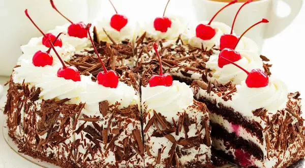 Una deliziosa foresta nera torta, ricoperta di panna montata e ciliegie rosse, con scaglie di cioccolato che la rendono irresistibile.