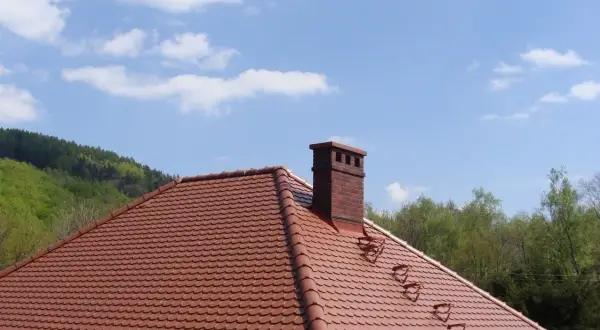 Solidna cegła klinkierowa na komin, dumnie wznosząca się nad czerwonym dachem.