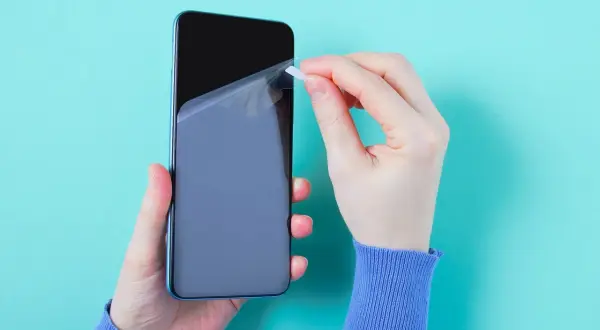 Ręce nakładają folię ochronną na ekran telefonu. Czy folia ochronna na telefon to dobry pomysł? Warto zabezpieczyć ekran.